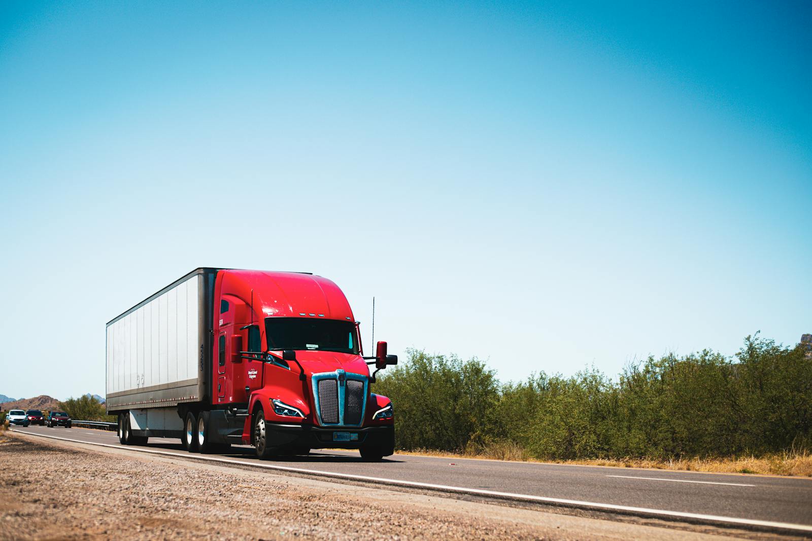 Vibrant red semi-trailer long haul truck driving on an open highway under a clear blue sky covered by high quality truck insurance