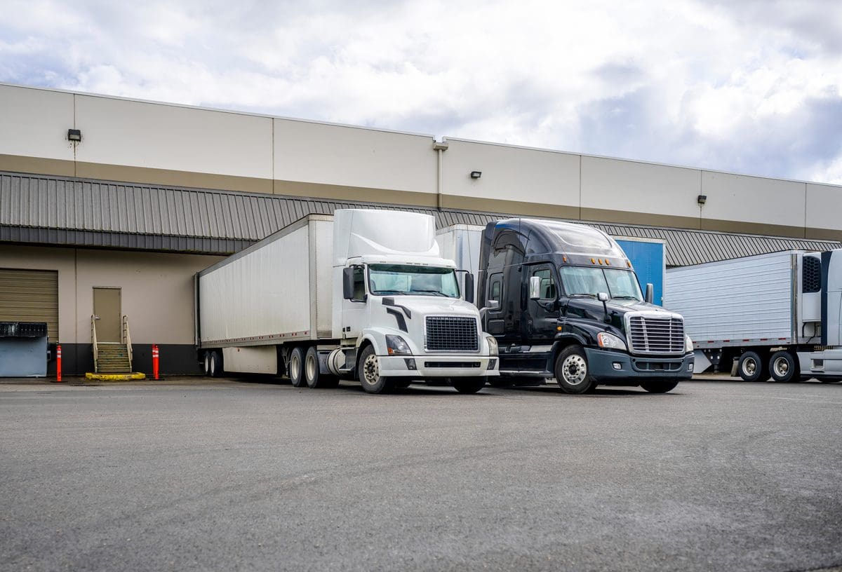 Two semi trucks at a warehouse loading dock, illustrating freight broker liability after the Montgomery ruling