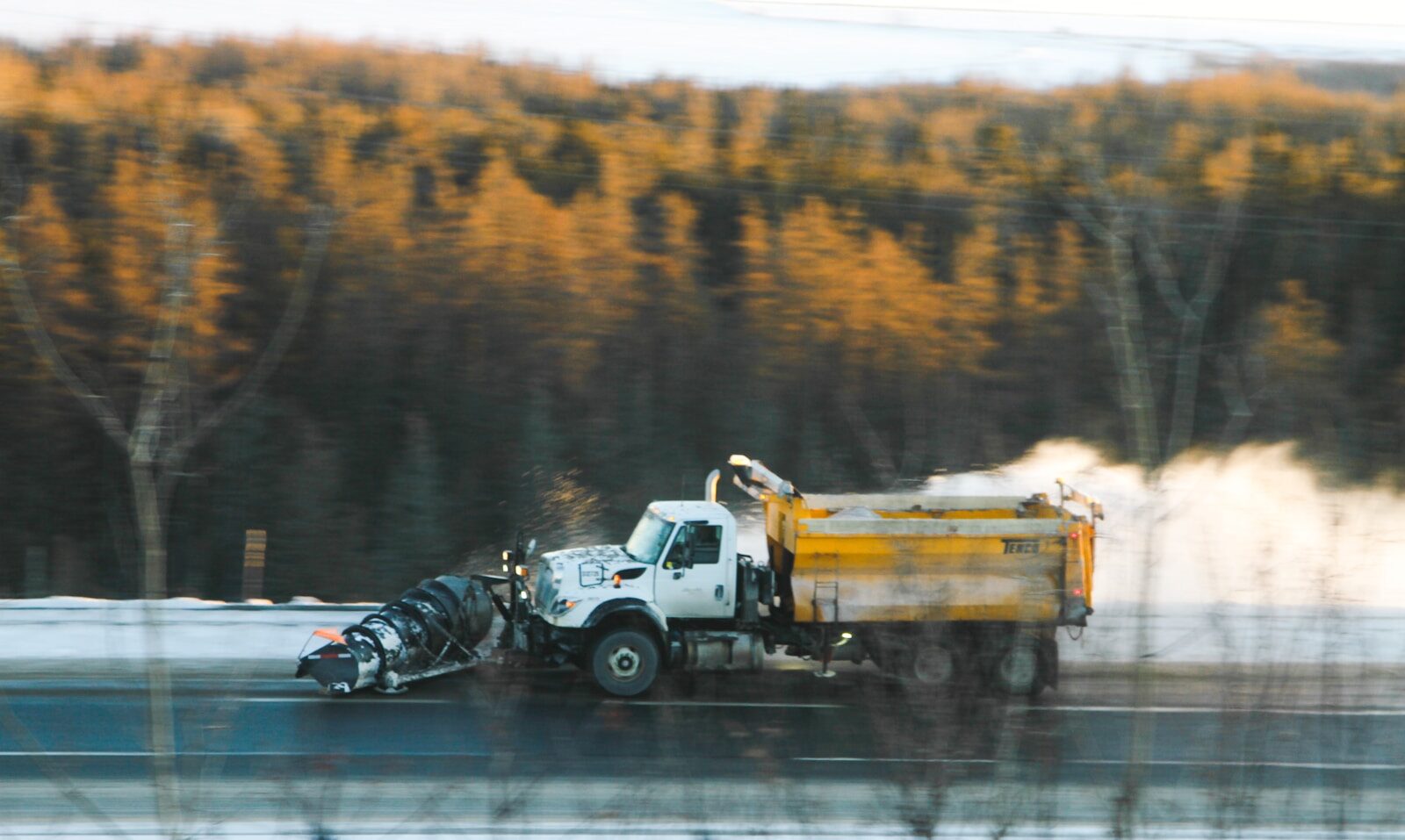 a dump truck driving down a road next to a forest