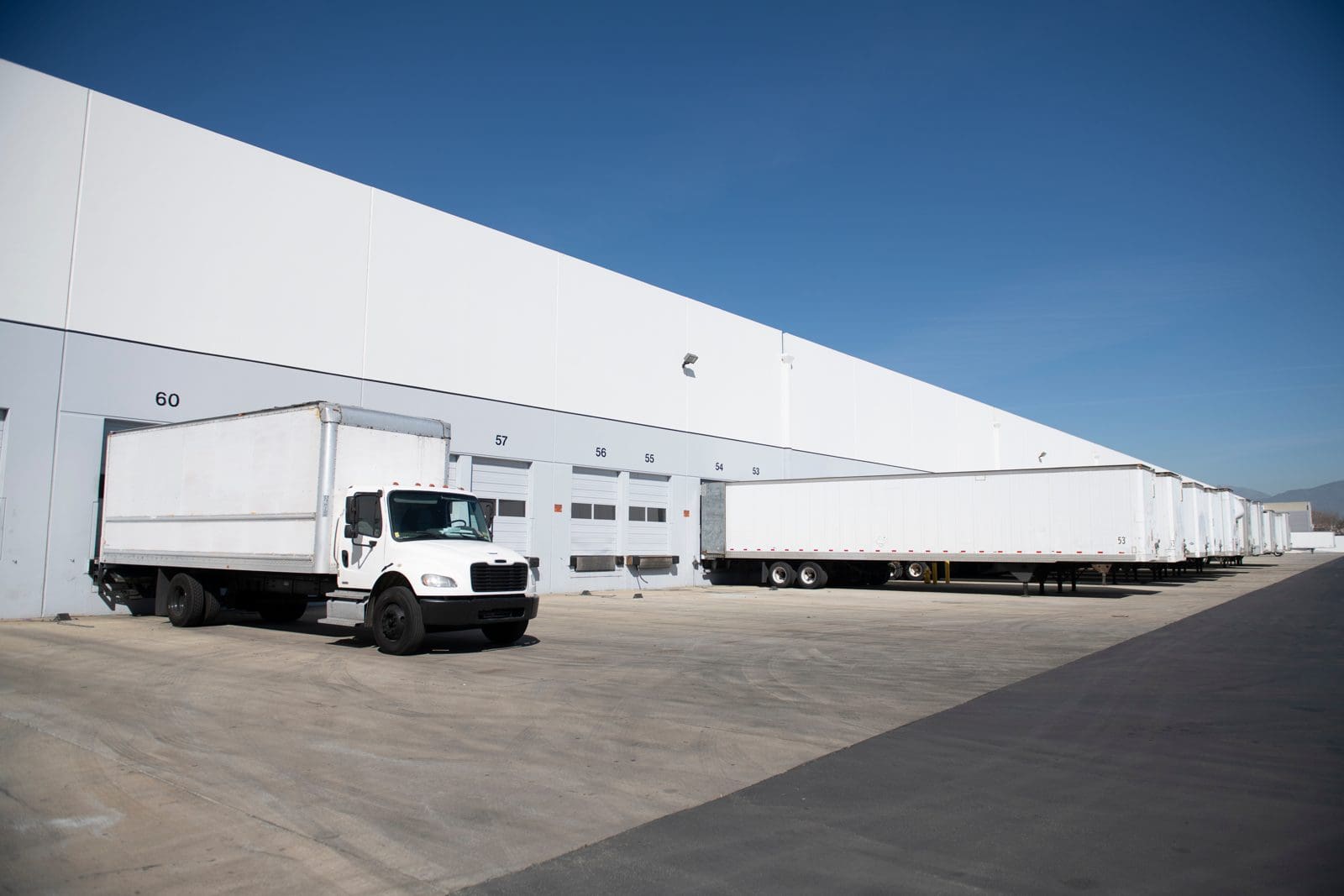 Box truck and trailers backed into a distribution center loading dock, the warehouse-to-warehouse freight Amazon Relay carriers haul