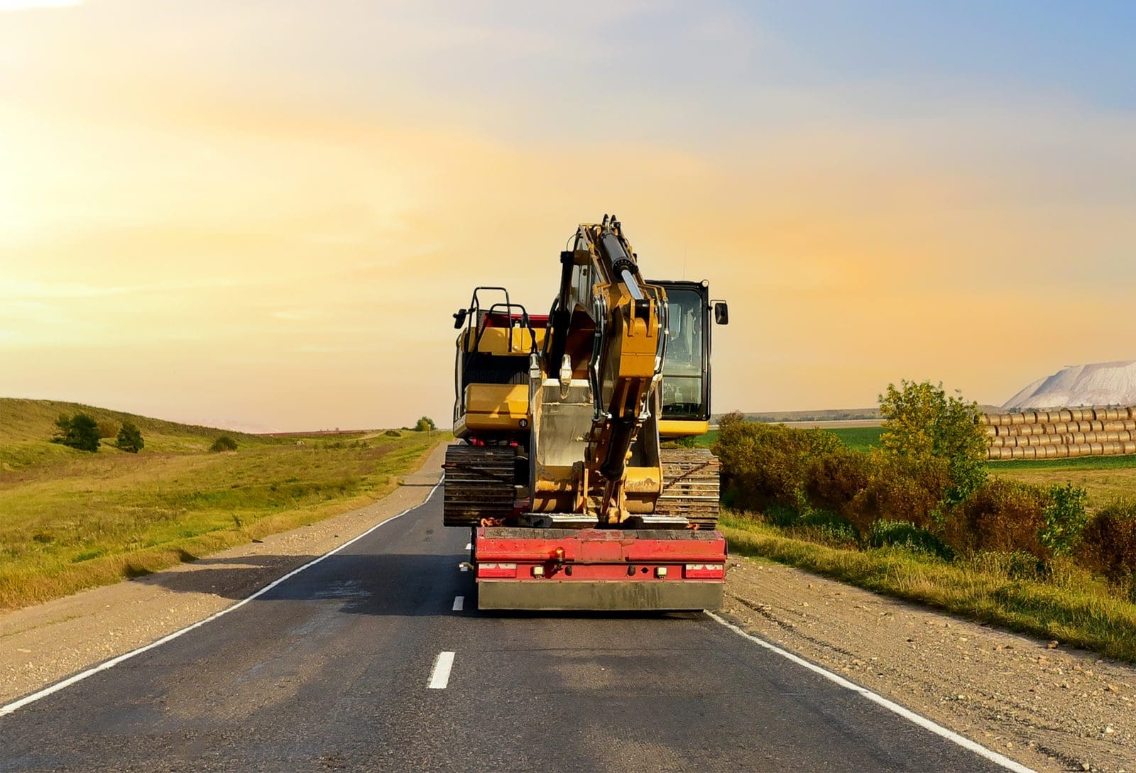 Semi truck hauling an excavator on a flatbed trailer, the kind of heavy machinery load that needs more than $100,000 in cargo insurance