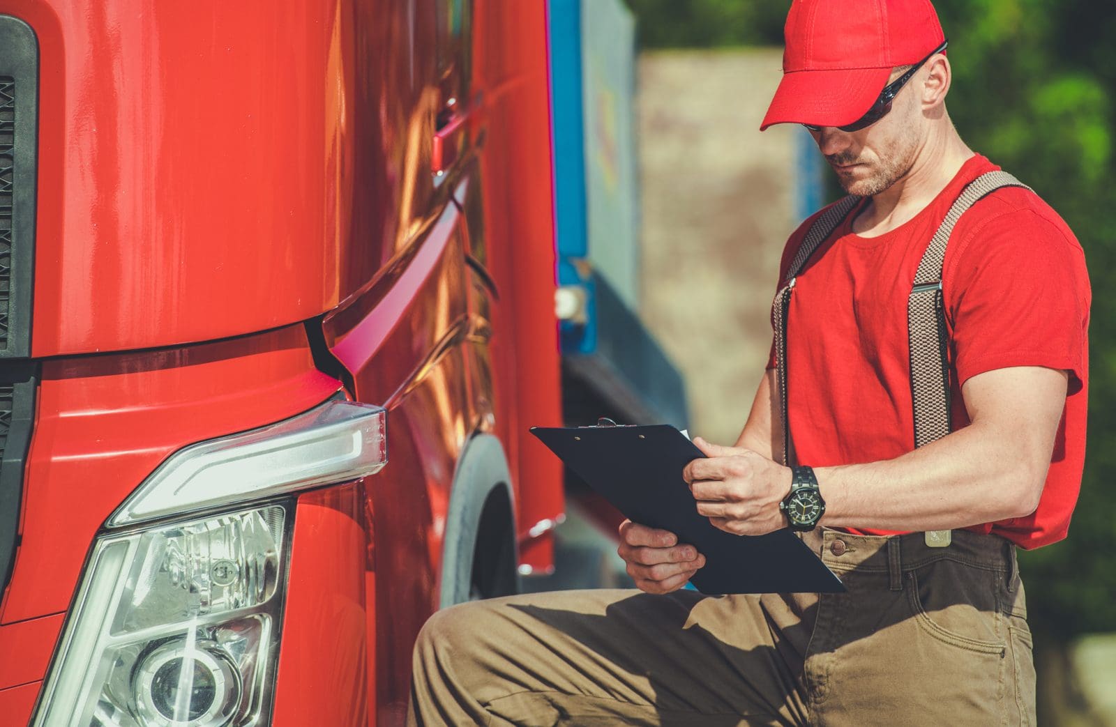 Truck driver reviewing paperwork beside a red semi truck before activating a new MC number